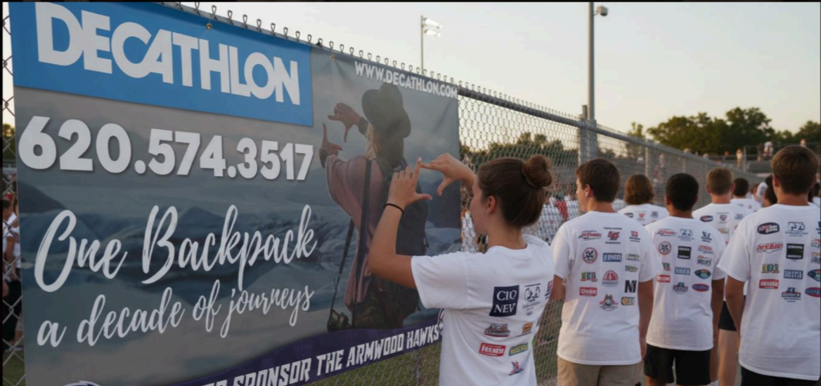 Students in spirit shirts next to a sponsor banner at a school event